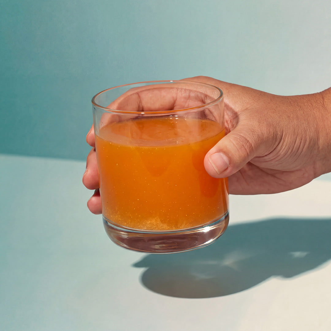 Image of a hand holding a glass containing a serving of Isotonix Essentials Anti-Aging